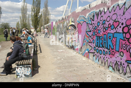 Blue sky nuvola bianca vista persone sedute sedi nella parte anteriore interna del muro di Berlino con colorati graffiti, Mauerpark, Berlino Foto Stock