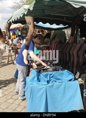 Ritratto Solare uomo organizzare pacchetti tabella alla pressione di stallo con pesce-net calze di nylon sul manichino gambe, Mauerpark Mercato delle Pulci, Berlino Foto Stock