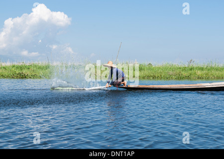 Fisherman squatting schizzi la superficie con remo per spaventare il pesce nella rete su 2 Novembre 2013 sul Lago Inle, Myanmar. Foto Stock