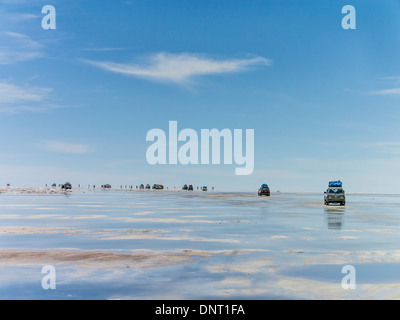 Turisti e quattro ruote motrici interrompere di prendere nel singolare interazione dei riflessi dall'acqua sul Salar de Uyuni. Foto Stock