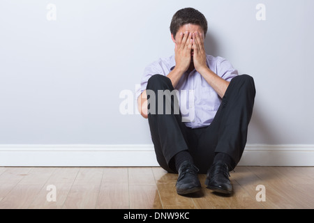 Imprenditore seduto sul pavimento con le mani che ricopre la faccia nella stanza vuota Foto Stock