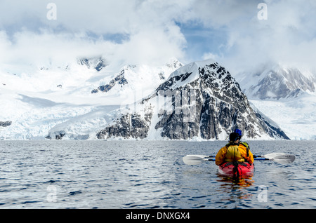 Antartide - Kayakers in un tandem kayak di mare dirigersi verso una ripida montagna rocciosa a Neko Harbour, l'Antartide. Foto Stock