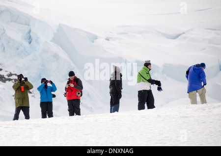Turisti Mikkelsen Harbour Trinity Island Antartide con gente / MIKKELSEN HARBOR, Antartide - i turisti della spedizione si trovano sul campo innevato sopra Mikkelsen Harbour a Trinity Island, Antartide, fotografando il ghiacciaio dietro di loro. Mikkelsen Harbour è un sito di sbarco gestito secondo le linee guida del trattato antartico che limitano le dimensioni dei gruppi a terra e richiedono rigorosi protocolli di biosicurezza per impedire l'introduzione di specie non native in una delle zone costiere più sensibili dal punto di vista biologico del continente. Foto Stock