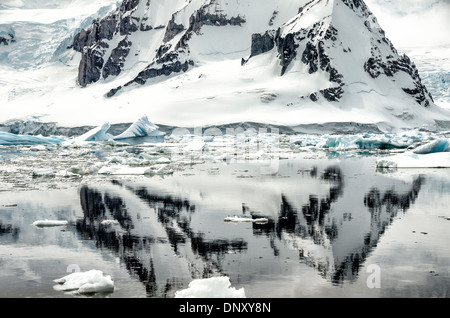 Antartide - una ripida montagna rocciosa è riflessa su acque calme come visto da de Cuverville Island sul lato occidentale della penisola antartica. Foto Stock