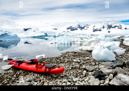 Antartide - un rosso brillante kayak tandem viene tirata in alto sulla costa rocciosa di de Cuverville Island, Antartide, con acque vetroso in background coperte con gli iceberg e appariscenti di ghiaccio. Foto Stock