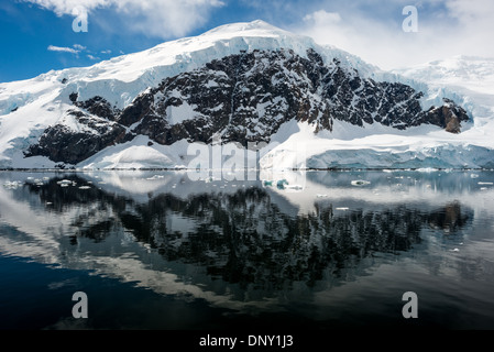 Neko Harbour Montagne innevate Riflesso dell'acqua Penisola Antartica | NEKO HARBOUR, Antartide — Un picco ghiacciato sulla costa Danco si erge sopra Neko Harbour, la sua faccia rocciosa scura striata di neve si riflette sull'acqua immobile della baia Andvord. La baia è stata mappata per la prima volta dalla Spedizione Antartica Belga del 1897-1899 sotto la guida di Adrien de Gerlache, e il porto stesso ha poi preso il nome da una nave fabbrica di caccia alle balene di Chr. Salvesen & Co. che vi ha ancorato dal 1911 al 1924. Foto Stock