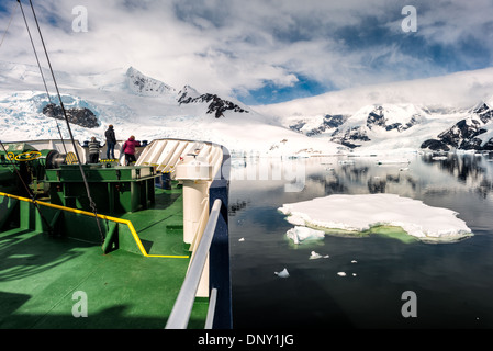 Antartide - un ice-nave rafforzato la navigazione attraverso il mare di ghiaccio e acque ancora a Neko Harbour sulla penisola antartica. La prua della nave polare (Pioneer) è a sinistra, con i passeggeri a guardare oltre la prua, con la montagna sulla riva in background. Foto Stock