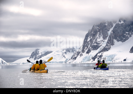 Kayakers paletta lungo in condizioni vetroso accanto a montagne panoramiche sul litorale vicino a Petermann Island sul lato occidentale della penisola antartica. Foto Stock