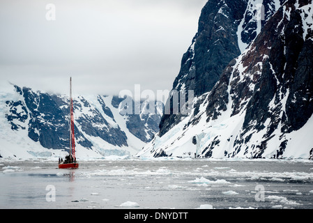 [Lemaire Channel Antartide] [Lemaire Channel Antarctic Peninsula] [Kyiv Peninsula] LEMAIRE CHANNEL, Antartide — Una barca a vela naviga con attenzione attraverso il ghiaccio lungo le ripide scogliere rocciose del Lemaire Channel. Questo stretto passaggio lungo la Penisola Antartica, soprannominato "Kodak Gap", presenta sfide uniche per le imbarcazioni a vela mentre manovrano attraverso le diverse condizioni di ghiaccio tra le torreggianti pareti del canale. Foto Stock