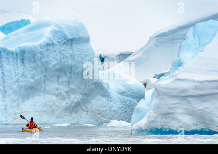 Iceberg Cemetery kayaker Melchior Island Antarctic Peninsula // Un kayak solitario naviga attraverso un'apertura tra grandi iceberg blu in un cimitero di iceberg in una baia di Melchior Island sulla penisola Antartica. Foto Stock