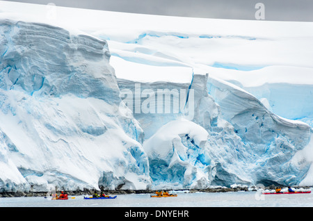 Antartide - Kayakers paddle passato massicce scogliere di ghiaccio del ghiacciaio lentamente scivolare in mare lungo il fronte mare di Melchior isola sulla costa occidentale della penisola antartica. Foto Stock