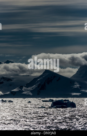 Stretto di Gerlache Montagne e ghiaccio Antartide | STRETTO DI GERLACHE, Antartide — Picchi innevati dell'Arcipelago Palmer si ergono sopra le acque riparate dello Stretto di Gerlache, con ghiaccio alla deriva sparso in primo piano. Mappato nel 1898 dalla Spedizione Antartica Belga sotto il tenente Adrien de Gerlache de Gomery, lo stretto si estende per circa 120 miglia (190 km) tra l'Arcipelago Palmer e la Costa Danco della Terra di Graham, protetto dalla Passaggio aperto di Drake. Foto Stock