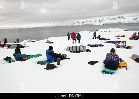 HUGHES BAY, Antartide: I turisti si accamparono sul ghiaccio e sulla neve a Hughes Bay, sulla penisola antartica, mentre un gruppo di pinguini Gentoo (Pygoscelis papua) riposano sul ghiaccio vicino al bordo dell'acqua. Questa scena cattura la convergenza unica di avventura umana e fauna selvatica in uno degli ambienti più remoti e incontaminati del mondo. Foto Stock