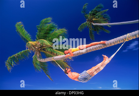 Giovane su Palm tree rilassante in amaca sopra la spiaggia di sabbia sotto il profondo blu del cielo Foto Stock