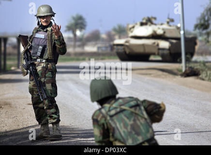 Feb 28, 2006; vicino a Ar Ramadi, Al Anbar, Iraq; un iracheno della polizia speciale Commando dal 2° Battaglione Brigata 2a, anche ampiamente noto come 'Wolf Brigata" parla di un compagno (sostenuto da un americano M1A1 Abrams serbatoio in background) in una zona rurale appena a nord della città irachena di Ar Ramadi su Feb 28, 2006. La polizia irachena sono stati su una missione congiunta con i soldati dal 101st airbour Foto Stock