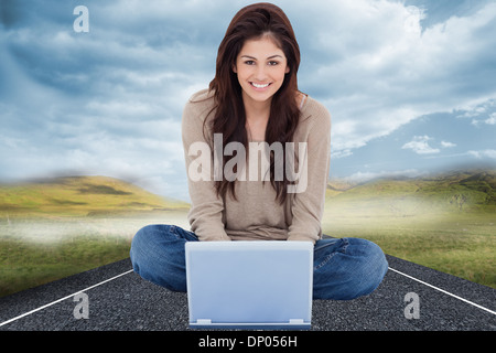 Immagine composita della donna seduta sul letto con il portatile di fronte a lei e sorridente Foto Stock