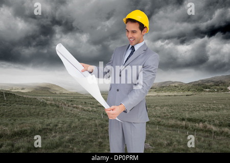 Immagine composita di sorridere architetto con elmetto guardando i piani Foto Stock