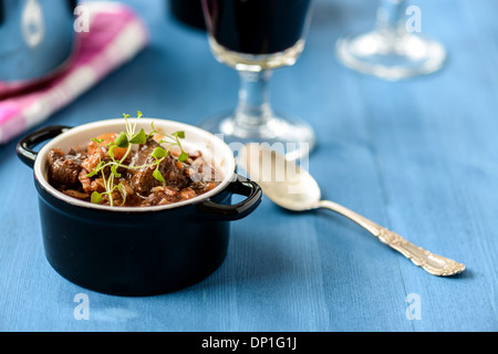 Boeuf Bourguignon classica francese stufato di manzo sul tavolo blu con un bicchiere di vino rosso Foto Stock