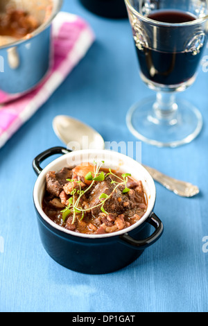 Boeuf Bourguignon classica francese stufato di manzo sul tavolo blu con un bicchiere di vino rosso Foto Stock