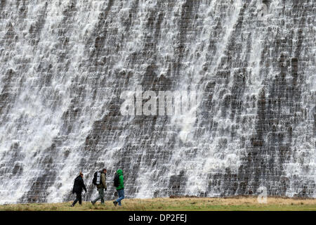 Il Peak District, Derbyshire, Regno Unito. Il 7 gennaio 2014. Dopo giorni di pioggia pesante, escursionisti sono sopraffatte da una parete d'acqua che trabocca dalla Derwent serbatoio sopra la diga Derwent nel Derbyshire Peak District. La diga è uno dei tre nella Derwent Vally che è stato reso famoso dalla Dambusters missioni di addestramento. Credito: Joanne Roberts/Alamy Live News Foto Stock