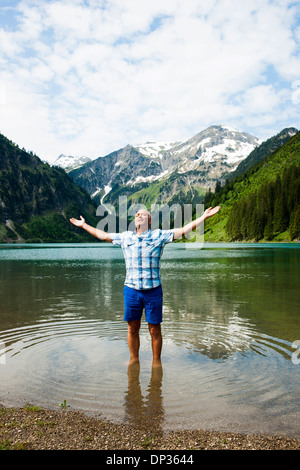 Uomo maturo con braccia tese verso l'esterno, in piedi nel lago Vilsalpsee, Valle di Tannheim, Austria Foto Stock