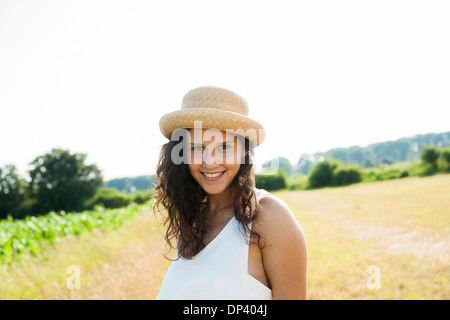 Ritratto di ragazza adolescente in piedi in campo, indossare un cappello di paglia, sorridente alla fotocamera, Germania Foto Stock