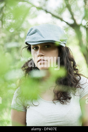 Close-up ritratto della ragazza adolescente che indossa il cappuccio esterno, guardando la telecamera attraverso foglie, Germania Foto Stock