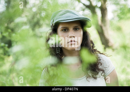 Close-up ritratto della ragazza adolescente che indossa il cappuccio esterno, guardando la telecamera attraverso foglie, Germania Foto Stock