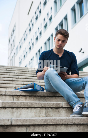 Giovane uomo seduto sui gradini esterni, utilizzando computer tablet, Germania Foto Stock