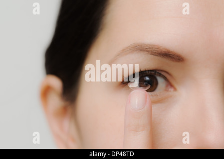 Donna che sta al posto di una lente a contatto nel Suo occhio Foto Stock