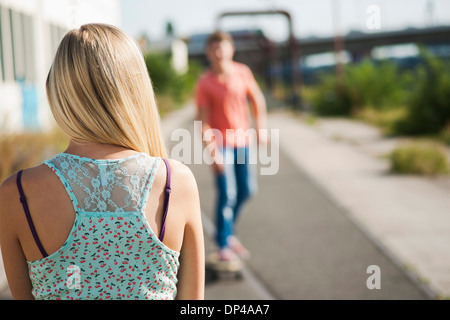 Backview della ragazza adolescente in primo piano e il ragazzo adolescente su skateboard in background, Germania Foto Stock