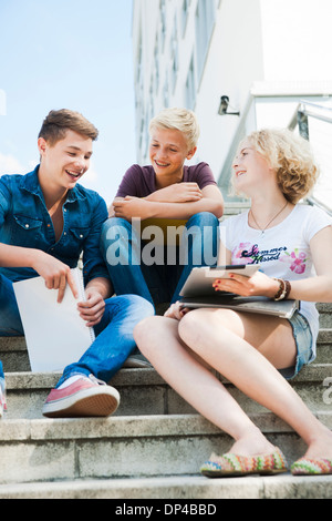 Gli adolescenti seduti sulle scale all'aperto, parlando e guardando il computer tablet, Germania Foto Stock