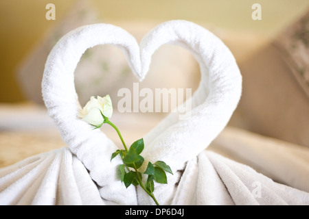 Due asciugamani bianchi cigni sul foglio di letto, decorato in rosa e cuore in camera di albergo Foto Stock