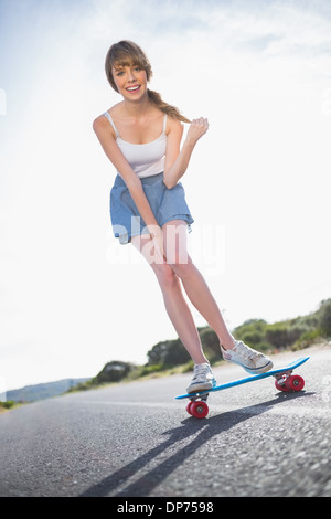 Allegro giovane donna il bilanciamento sul suo skateboard Foto Stock