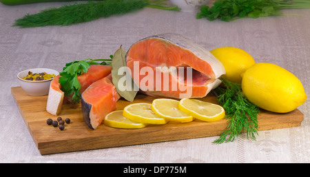 Sul tavolo sono tagliati in pezzi grandi di pescare il salmone, limone, aneto, prezzemolo e spezie per cucinare il pesce. Foto Stock