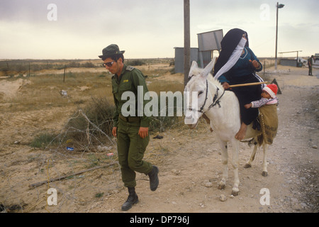 Rafah Crossing 1980S.. Donna beduina con un bambino che cavalca un asino e soldato israeliano al nuovo attraversamento che sta attraversando da un soldato israeliano. Quando Israele si ritirò dal Sinai nel 1982, Rafah fu diviso in una parte di Gazan e una parte egiziana, dividendo le famiglie, separate da barriere a filo spinato. Il nucleo della città fu distrutto da Israele ed Egitto per creare una grande zona cuscinetto. Rafah, palestinese, Striscia di Gaza, aprile 1982. HOMER SYKES Foto Stock