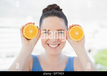 Sorridente donna slanciata in azienda di abbigliamento sportivo di fette di arancia Foto Stock