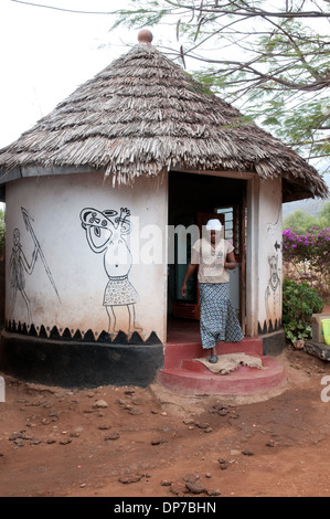 Fango e bargiglio rondavel con tetto di paglia e fantasiosa arte africana opera murale a duka tappa turistica Namanga Kenya Africa Foto Stock