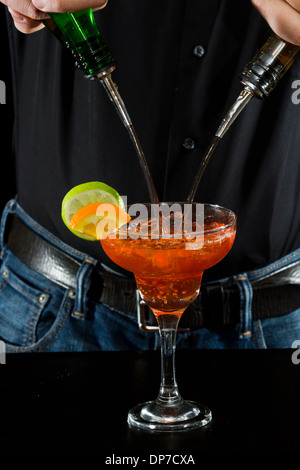Azione girato di un barman versando red margarita utilizzando più bottiglie Foto Stock