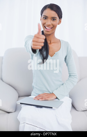 Allegro attraente donna seduta sul divano accogliente dando pollice in alto Foto Stock