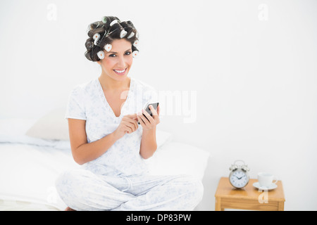 Felice bruna nei capelli rulli inviando un testo sul letto Foto Stock