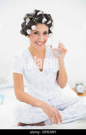 Felice bruna nei capelli rulli tenendo un bicchiere di acqua Foto Stock