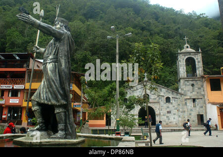 26 nov 2006 - Aguas Calientes, Perù - La statua di bronzo di un sovrano inca punti una direzione mentre peruviani locali a piedi l'altra direzione, passando da uno stile coloniale della Chiesa Cattolica, nella città appena sotto le antiche rovine Inca di Machu Picchu in Vilcabamba la gamma della montagna nel sud del Perù. Le rovine sono state a casa per la elevata righelli Inca e sacerdoti e ora portare in thousan Foto Stock