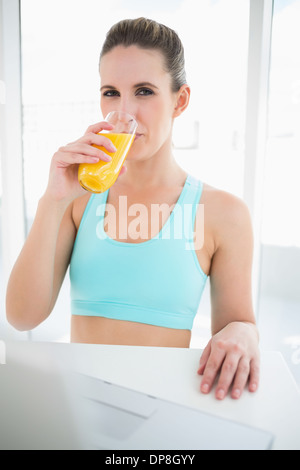 Donna che indossa abbigliamento sportivo di bere succo di arancia Foto Stock