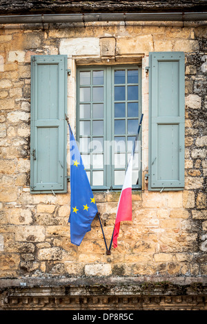 Domme, Dordogne, la Francia, l'Europa. Ue & bandiere francese di fronte a una vecchia finestra con persiane in legno. Foto Stock