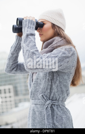 Donna Gorgeous con abbigliamento invernale a guardare attraverso il binocolo Foto Stock