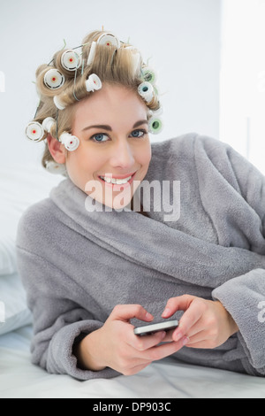 Gioioso rilassato donna bionda in arricciacapelli utilizzando il suo telefono cellulare Foto Stock