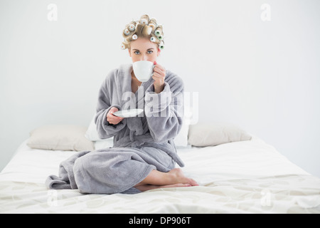 Attraente rilassato donna bionda in arricciacapelli a bere caffè Foto Stock