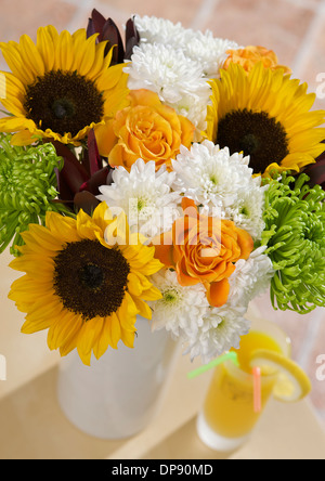 Girasoli, Marie Claire Roses arancio, Anastasia verde lime, Crisantemi bianchi e gambi di Leucadendron maroon in un vaso in un ambiente domestico Foto Stock