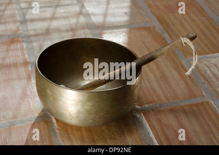 Un tibetano Singing Bowl seduta su un pavimento piastrellato con un testimone in appoggio all'interno. Foto Stock